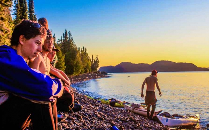 a group of outward bound students rest on the shore of blue lake after a day of kayaking